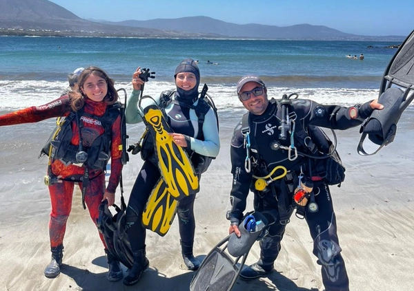 Tres buzos con el equipo en la playa al salir del agua
